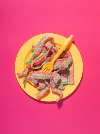 Rainbow sour belts in a yellow plate, on bright pink background, top view. Food concept, excessive...