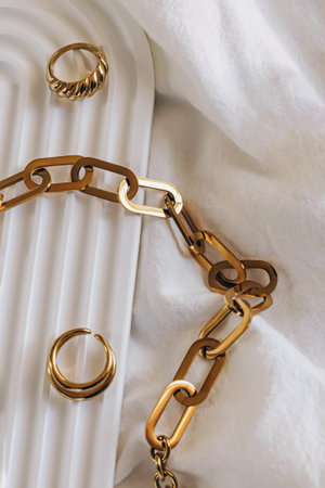 Golden chain necklace and ring on geometric tray, minimal jewelry still lifeの写真素材