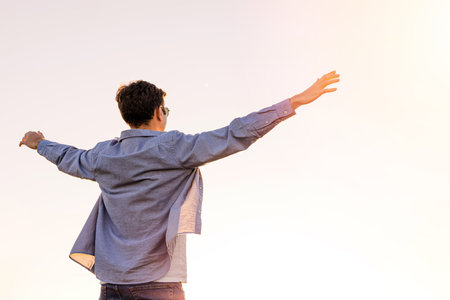 Man standing with his hands rised towards the sun in a warm sunset lightの写真素材