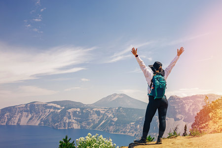 Woman standing with her hands rised after a hike on the top with a view to a picturesque lakeの写真素材