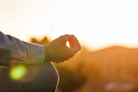 Close-up of male hand in meditation pose in warm sunset light, meditation and mindfulness conceptの写真素材