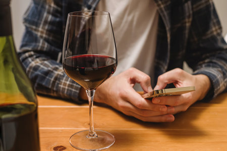 Close-up shot of a man with a glass of wine and holding a phone to track amount of alcohol or to a wine in an app. Mindful drinkingの写真素材