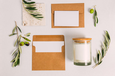Blank paper card, envelope and candle with blank space. Flat lay composition with olive branches....