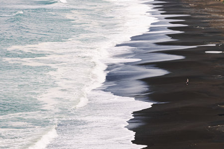 Big waves rolling on the beach with two unrecognizable people standing in the distanceの写真素材