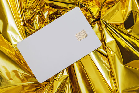 White blank credit card with chip lying on the golden foil background, mock-upの写真素材