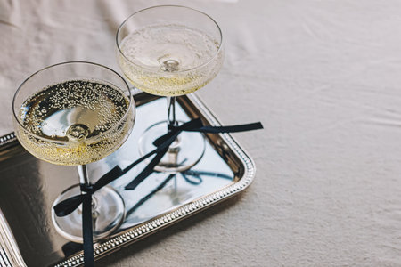 Two coupe glassed with sparkling wine decorated with satin ribbon bows standing on elegant silver trayの写真素材