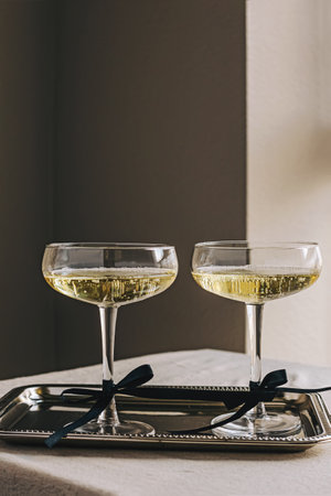 Two coupe glassed with sparkling wine decorated with satin ribbon bows standing on elegant silver trayの写真素材