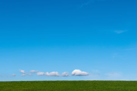 Small clouds over horizon over green grass hillの写真素材