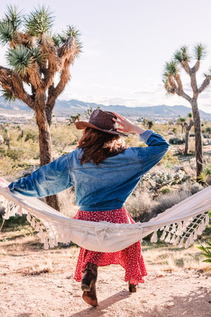 Woman sitting in hammock among Joshua trees, boho vibes and desert lifestyle