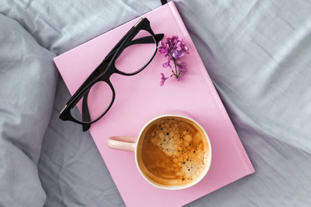 Composition with pink mug with coffee, pink notepad or diary and glasses on the bed, overhead viewの写真素材