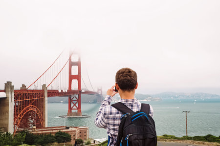 Tourist with a backpack Taking Pictures of Golden Gate Bridge on Foggy Day Near San Francisco Bay