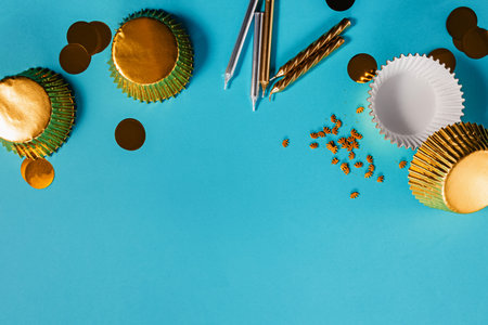 Festive birthday party decoration and supplies in golden color on a bright blue backdrop with cupcake liners, confetti, and candlesの写真素材