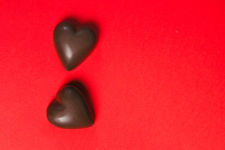 Two dark chocolate hearts sit on a bright red background, Valentineâs Day celebrationの写真素材