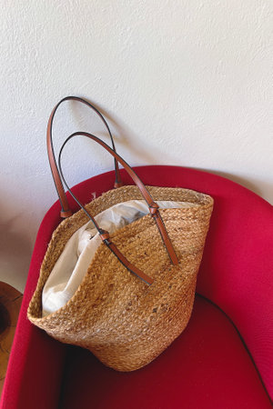 Stylish summer woven bag standing on vibrant plush pink chair in a modern living spaceの写真素材