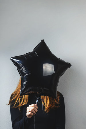 Unrecognizable person holding a black star-shaped balloon while standing against a neutral wall indoorsの写真素材