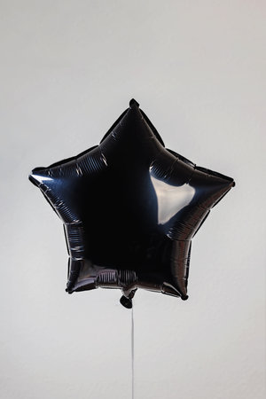 A single black star-shaped balloon floating against a plain grey backgroundの写真素材