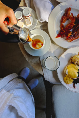 Enjoying a relaxing breakfast with coffee, bacon, and eggs in a cozy settingの写真素材