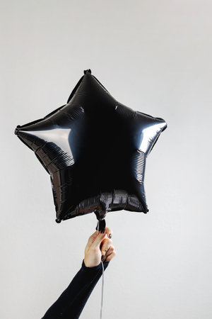 Hand holding a black star-shaped balloon against a minimalistic gray background during a festive celebrationの写真素材