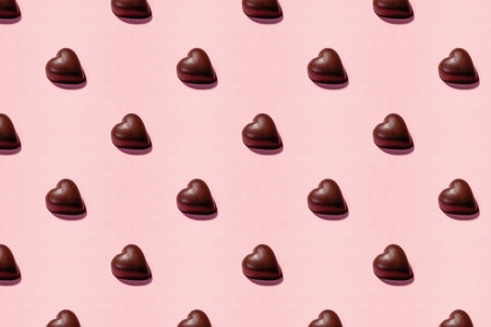 Heart-shaped chocolate pieces arranged on a soft pink background, creating a romantic patternの写真素材