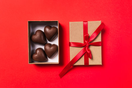 A beautifully wrapped box with a red ribbon with heart-shaped chocolates on a red background, romantic Valentine's day giftの写真素材