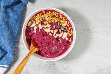 Bright and creamy berry smoothie bowl topped with granola and almonds on stone tableの写真素材
