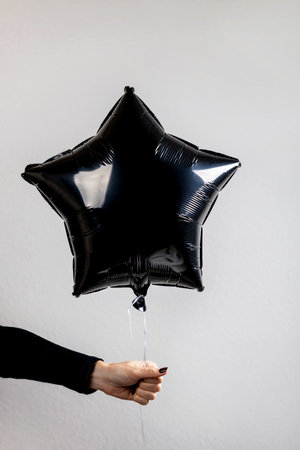 Hand holding a black star-shaped balloon against a minimalistic gray background during a festive celebrationの写真素材