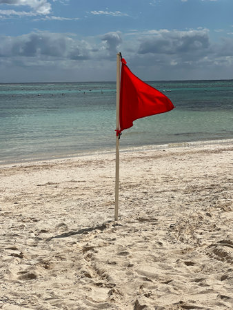 Red warning flag stands on sandy beach indicating hazardous water conditions during sunny dayの写真素材
