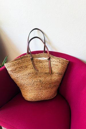 Natural straw bag placed on a bright pink chair in a cozy indoor settingの写真素材