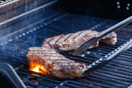 Close-up view of two juicy steaks sizzling on the hot outdoor grillの写真素材
