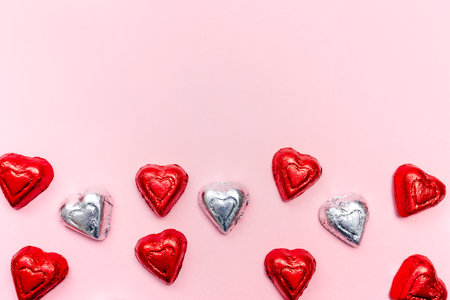 Colorful heart-shaped chocolates arranged in a playful pattern on a pink background for Valentine's day celebrationの写真素材