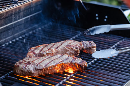 Two thick steaks sizzle over an open flame on a backyard grill, close-up viewの写真素材