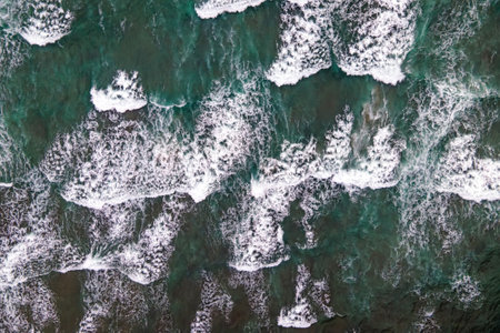 Turquoise waves break upon dark rocks along the shore, aerial viewの写真素材
