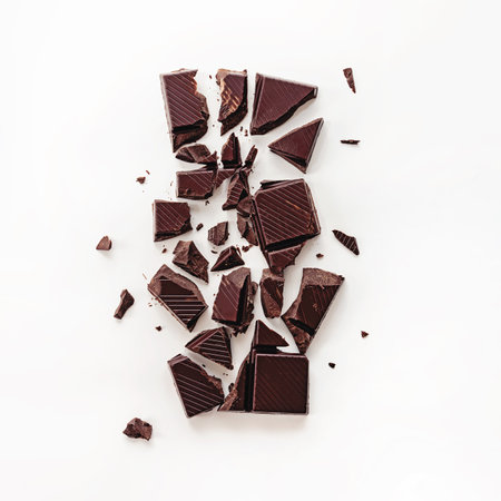 Dark chocolate chunks are broken and scattered over a plain white surface, showcasing their rich texture and deep color.の写真素材