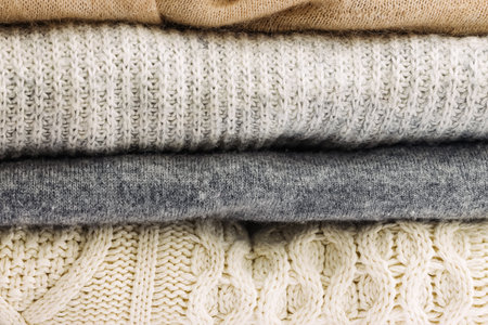 A stack of cozy knitted sweaters in neutral colors, showcasing various textures and patternsの写真素材