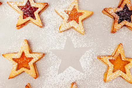 Star-shaped cookies filled with various jams are arranged on a baking sheet, dusted with powdered sugar. The cookies create a festive and inviting display, perfect for holiday celebrations.の写真素材
