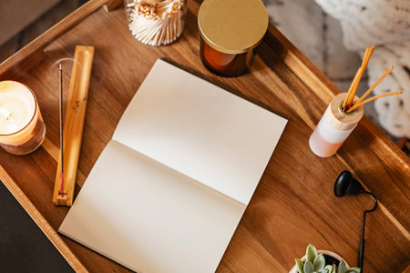 Workspace for journaling or meditation with an open notebook on a wooden tray surrounded by scented candles, incense, and a small plantの写真素材