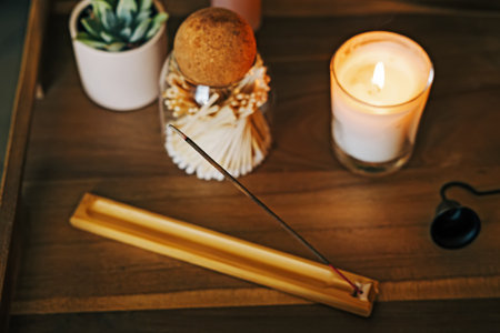 A cozy setup featuring a burning incense stick in a holder next to a lit candle, creating a serene and aromatic atmosphere.の写真素材