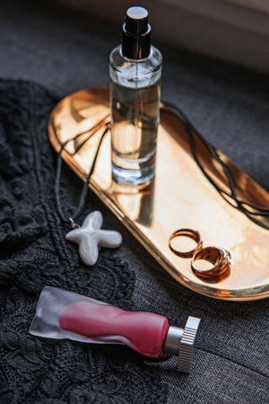 A stylish arrangement of a perfume bottle, rings, and a necklace on a golden tray over a dark lace fabric.の写真素材
