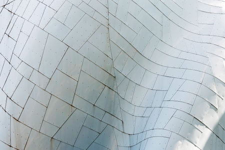 Abstract close-up of curved metal facade with tiled panels, seams, and rivets; modern architecture...