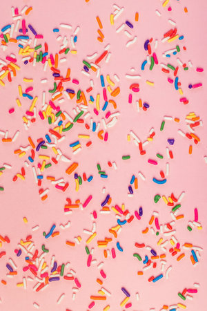 A vibrant assortment of colorful sprinkles scattered across a pink surface, creating a playful and festive pattern perfect for celebrations and dessert themes.の写真素材