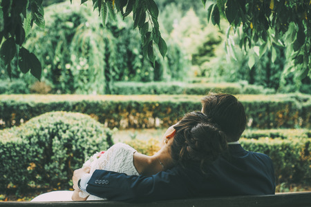 couple is sitting on the bench hugging in the green parkの写真素材