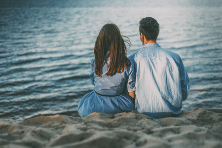 couple is sitting on the sand coast together watching on the blue sea with sunlight sunsetの写真素材