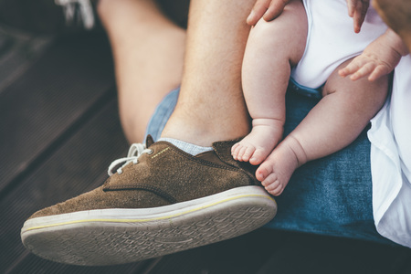 two small cute newbord kid legs with father in brown sport shoesの写真素材
