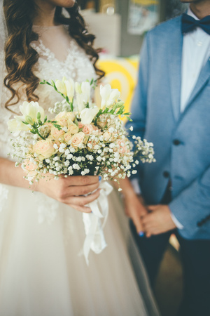bride and groom staying together with bouquet in hands in dress and blue suitの写真素材
