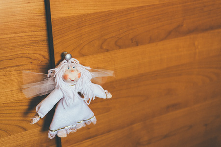 Cute handmade fabric doll is hanging on the chestnut brown wooden closetの写真素材