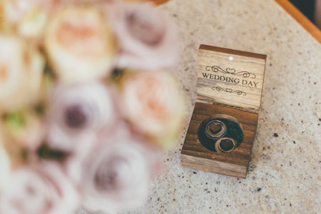 Blurred rose wedding bouquet in front and wooden box of silver wedding rings behind