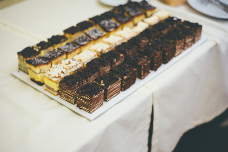 Delicious snacks in form of different sharp edged cakes are standing on a table, which is covered with white decor rugの写真素材