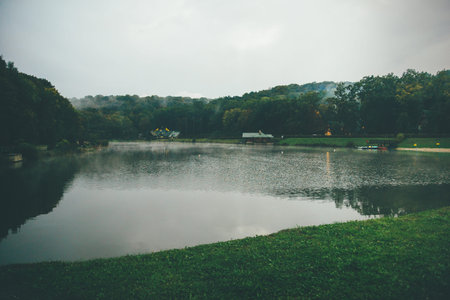 Mysterious lake and fall trees in hazy atmosphere, some buildings here and there also covered in...