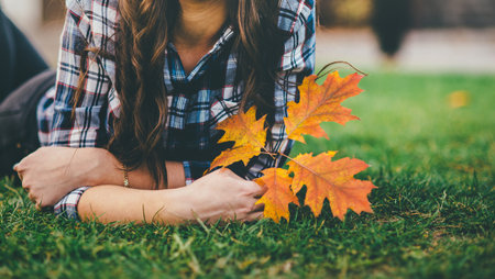Noface photo of a brunette laying on the trimmed grass with golden autumn leave in her hand