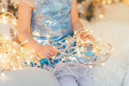 Closeup of a girl in a blue dress holding Christmas fairylights while sitting on the white fluffy rugの写真素材